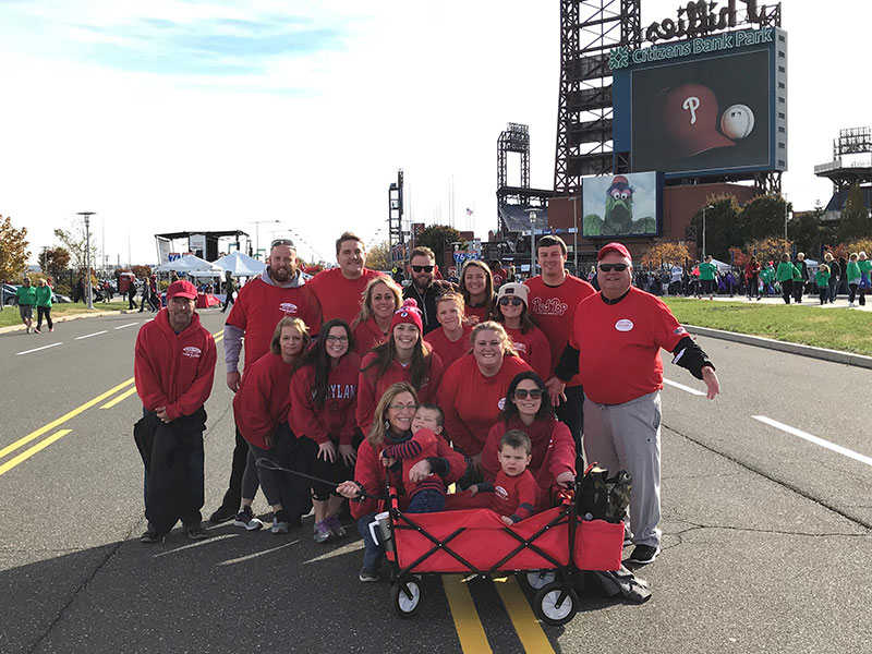 A group of people wearing red shirts smiling at the camera in front of a baseball stadium.