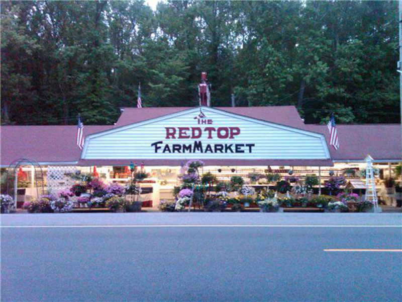 Front view of Red Top Farm Market's exterior. A white building with a red roof and red lettering saying "The Red Top Farm Market."