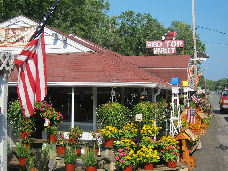 Side view of the outside of Red Top Farm Market featuring the sign and a variety of flowers in pots and hanging baskets.
