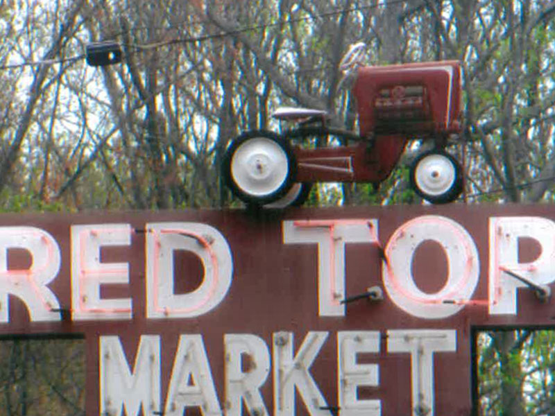Red Top Farm Market's red and white sign featuring a red tractor on top. 