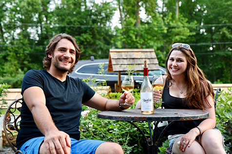 A man and woman sitting at a table and smiling at the camera while holding wine glasses from Sharott Winery.