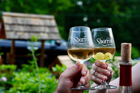 Two Sharrott Winery wine glasses clinking together in front of Red Top Farm Market.
