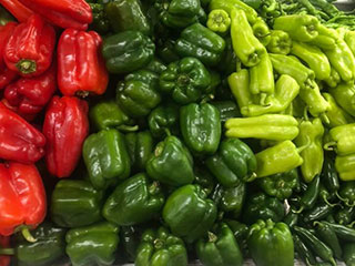 A huge pile of red and green bell peppers and a pile of light green sweet peppers.