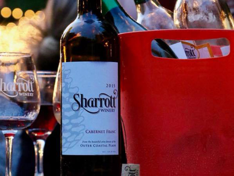 Closeup of a Sharott Winery wine glass, Cabernet Franc wine bottle, and a red raffle prize bucket
